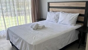 Una cama bien tendida con sábanas y almohadas blancas, un cabecero de madera y una mesita de noche con una lámpara.