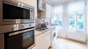 Eine moderne Küche mit Edelstahlgeräten, einem Backofen, einer Mikrowelle, einem Gasherd und einer integrierten Waschmaschine.
