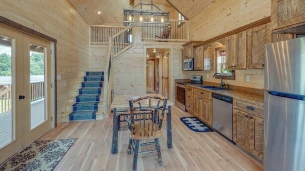 Ein Holzblockhaus-Interieur mit einer Treppe, die zu einem Balkon, einem Essbereich und einer Küche mit modernen Geräten führt.