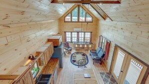 Ein geräumiges Blockhaus mit hohen Decken, Holzwänden, einer zentralen Sitzecke und einem großen Fenster für natürliches Licht.