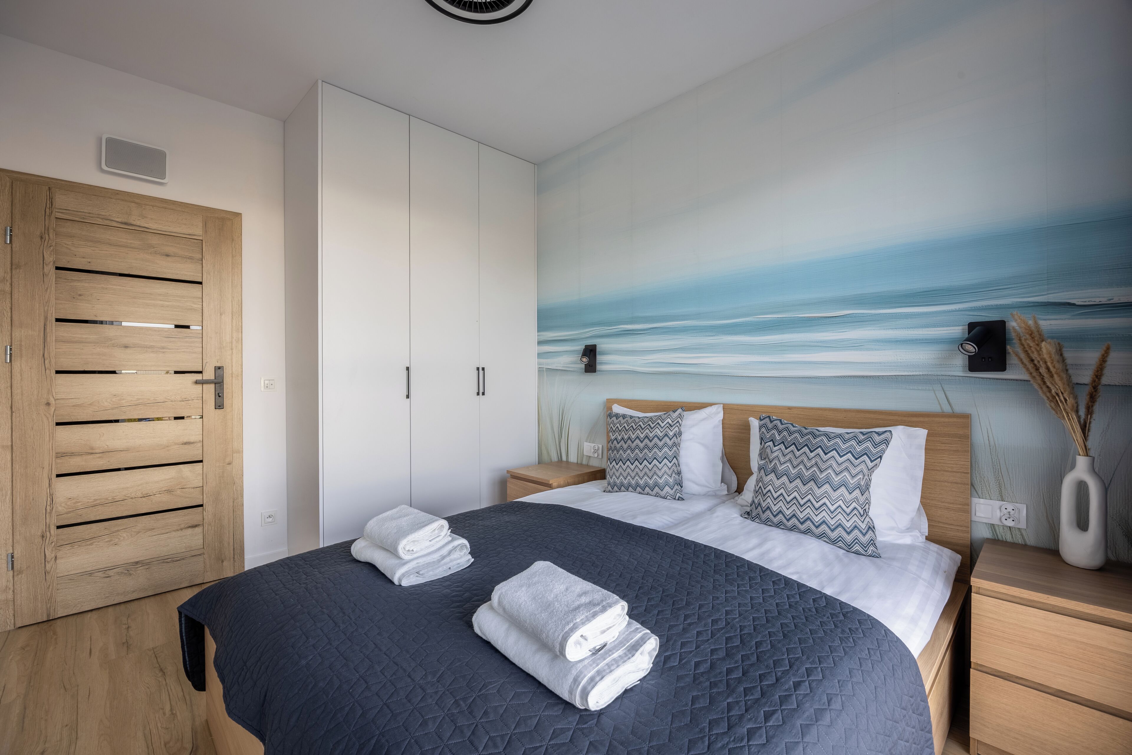 A bedroom with a bed, wooden wardrobe, and a wall mural of a beach.