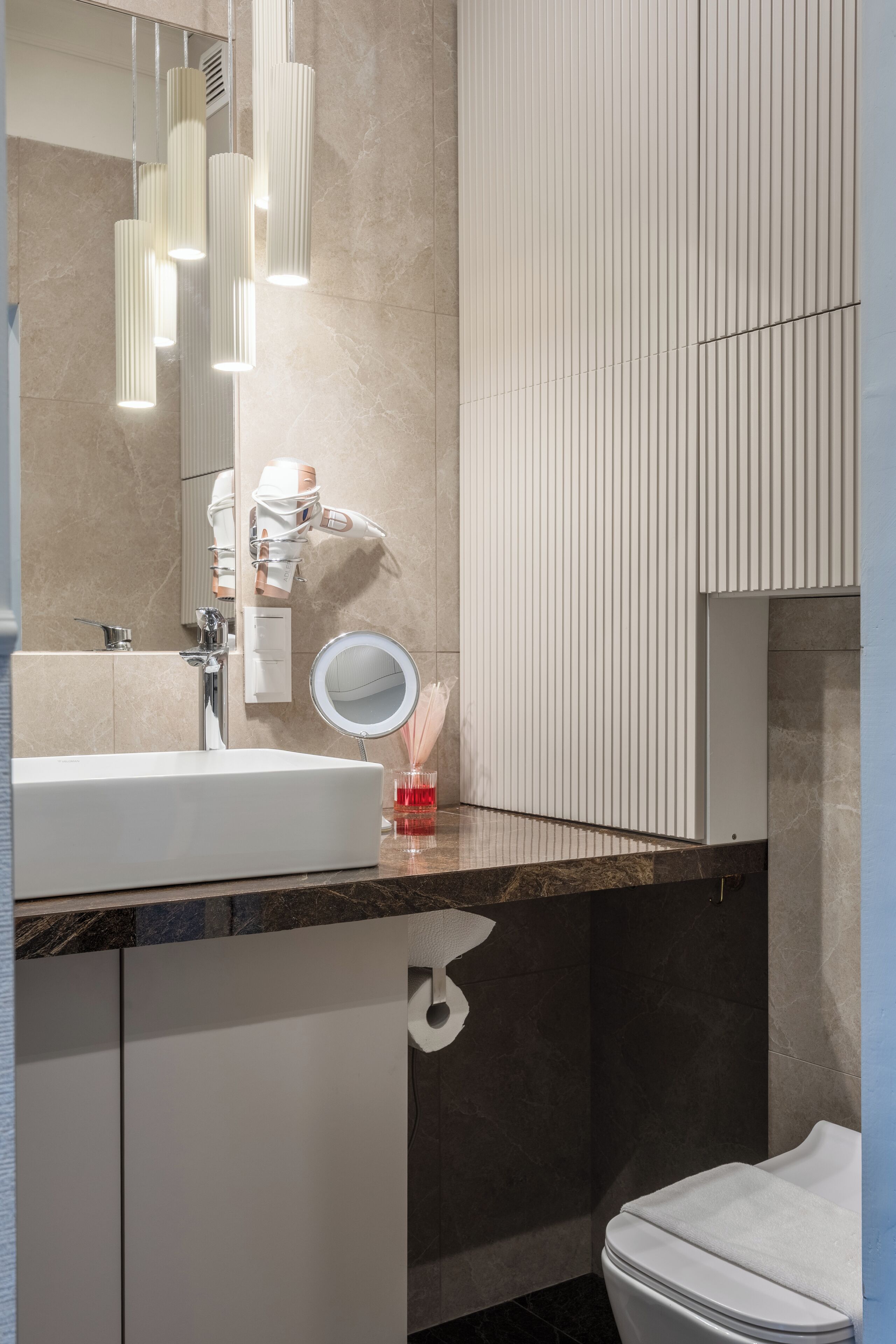 Un baño moderno con un lavabo blanco, un espejo y un perchero para toallas.