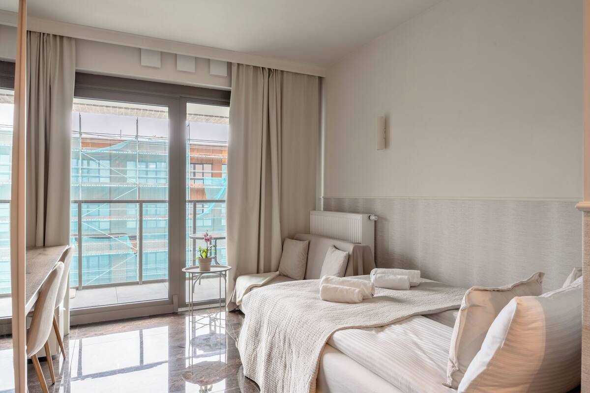 A hotel room with a large window, a bed, a bedside table, and a chair.