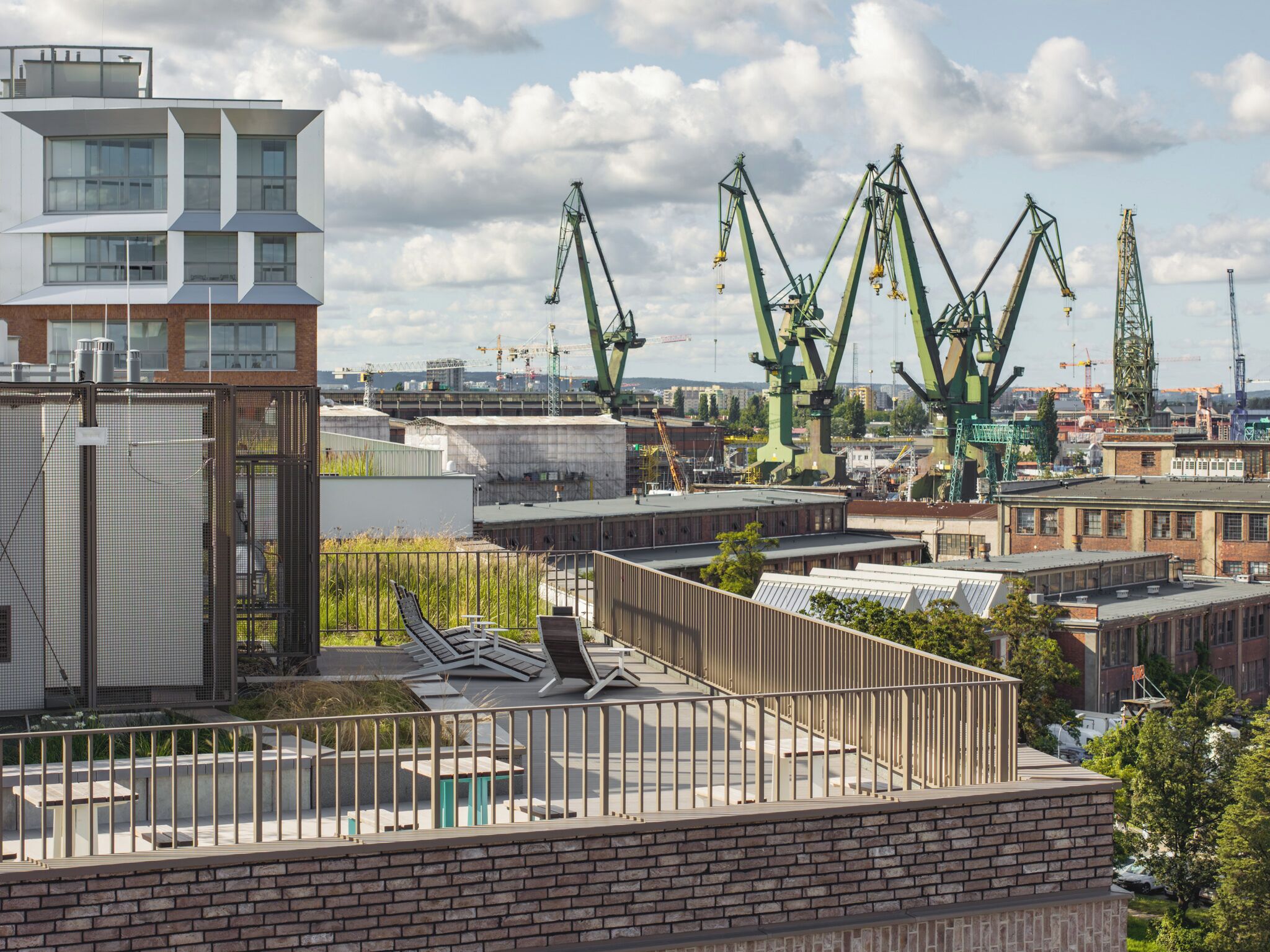 A rooftop terrace with a view of industrial cranes and buildings.