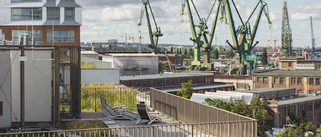 A rooftop terrace with a view of industrial cranes and buildings.