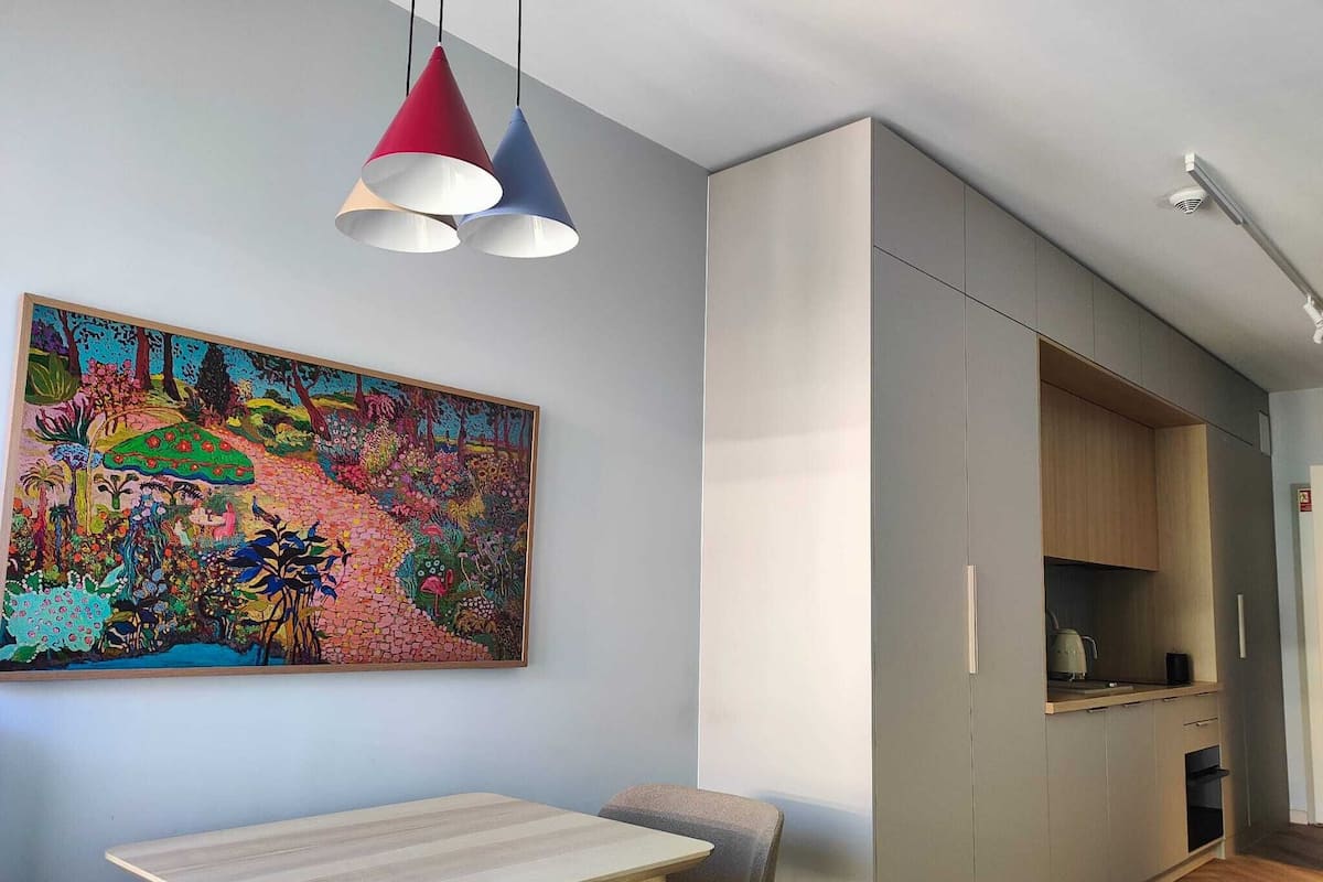 A modern kitchen with built-in cabinets, a dining area with a table and chairs, and a colorful abstract painting on the wall.