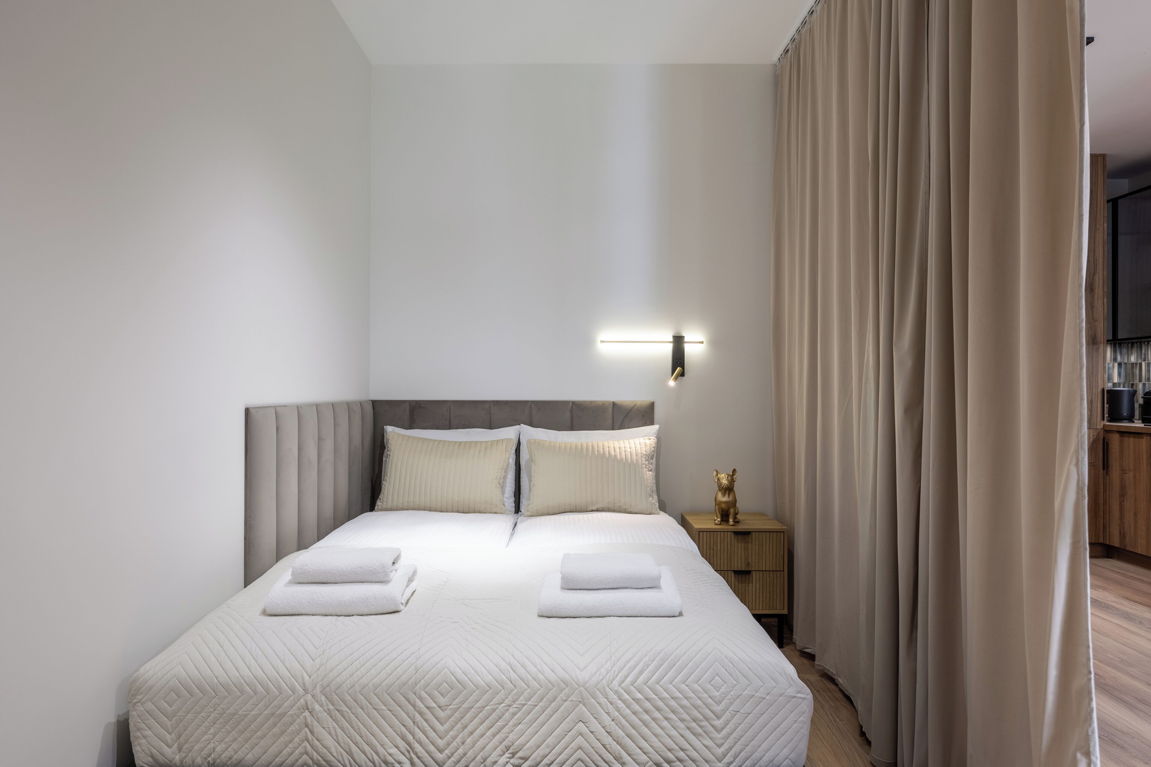 Un lit bien fait, avec des oreillers et une couverture, une table de chevet avec une lampe et un rideau.