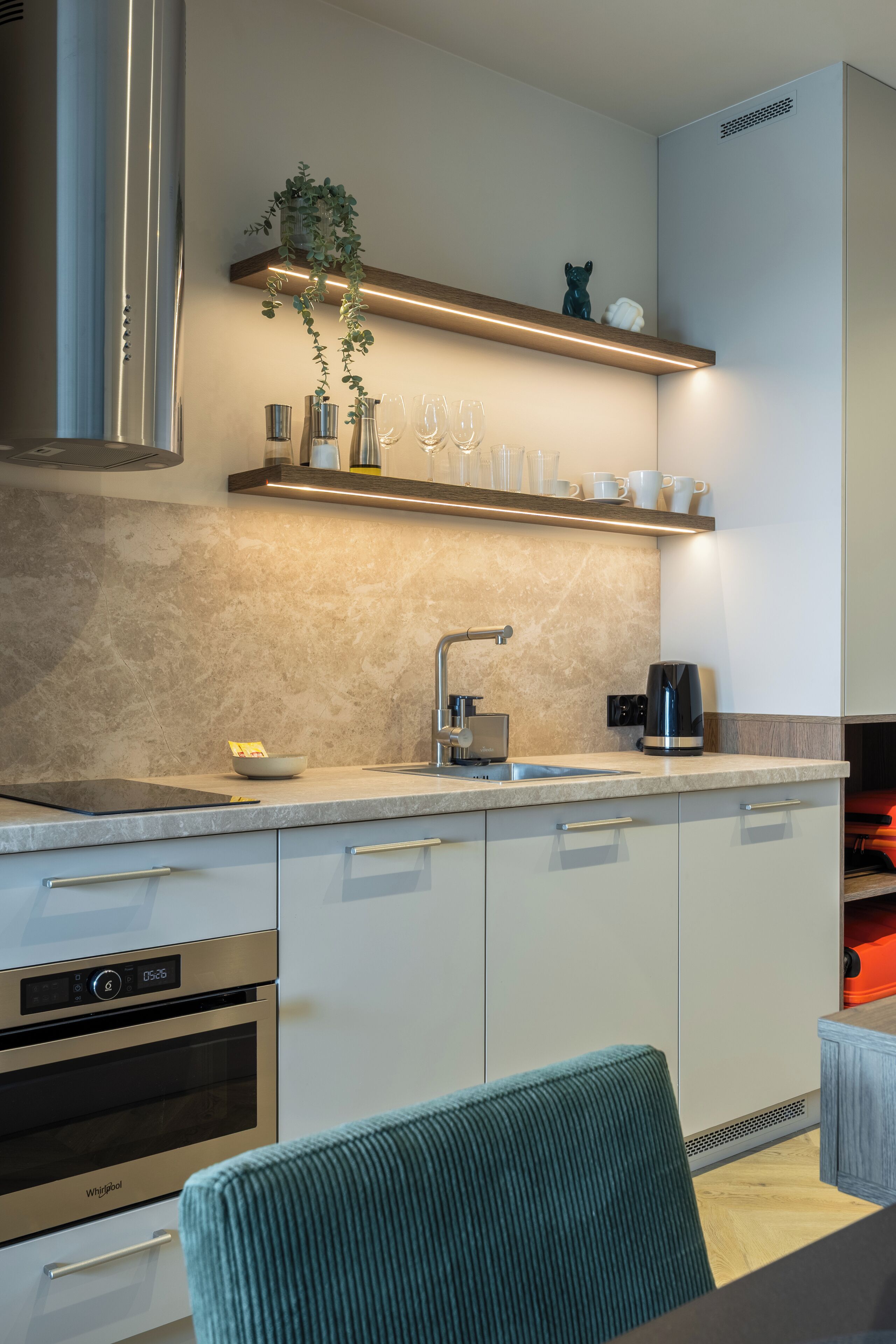 A modern kitchen with a built-in oven, a stainless steel range hood, a countertop with a coffee maker, and a hanging plant.