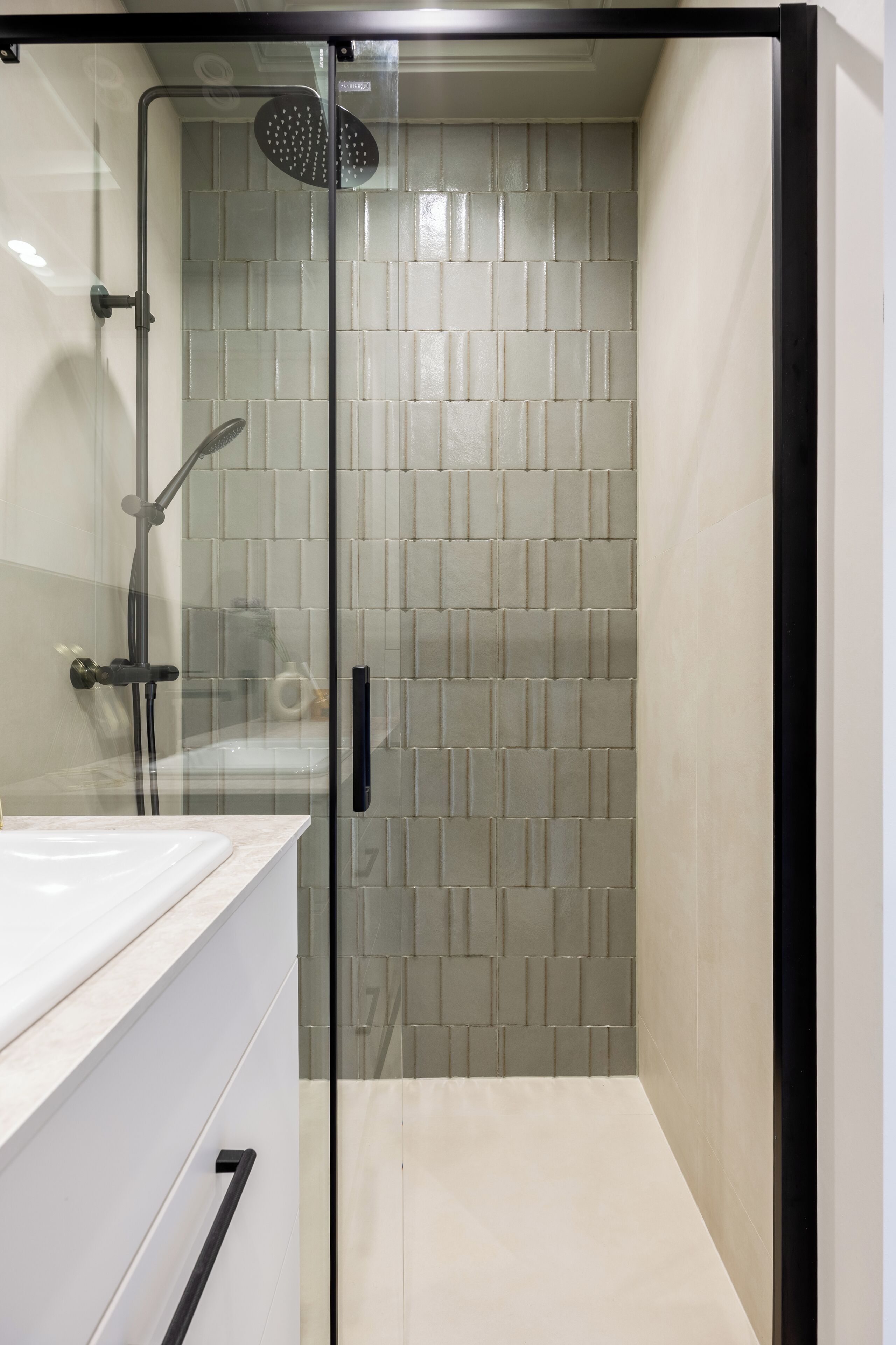A modern bathroom with a glass-enclosed shower, tiled walls, and a white countertop.
