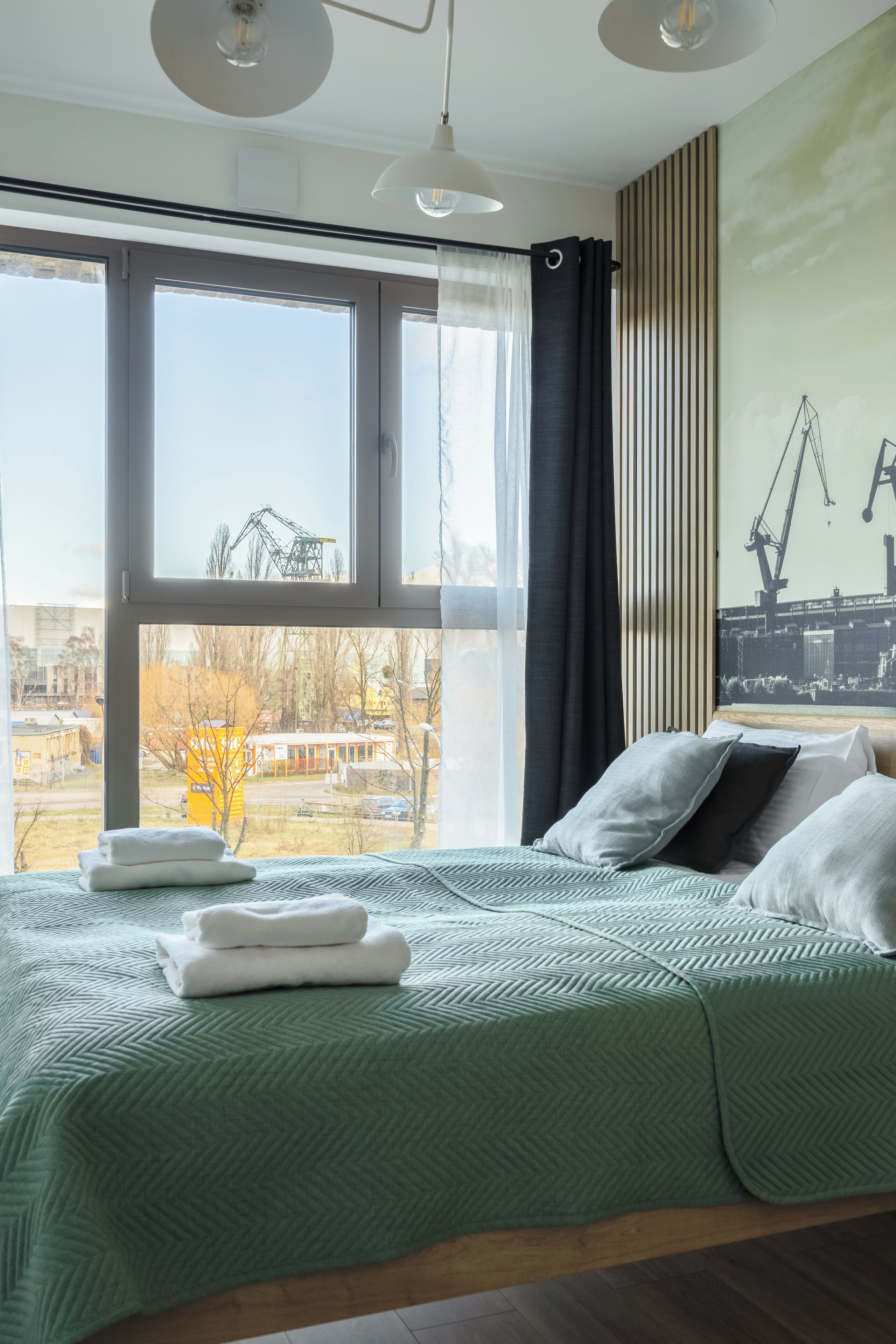 Een moderne slaapkamer met een groot raam, een bed met een bedovertrek met groen patroon, en een uitzicht op de stad.
