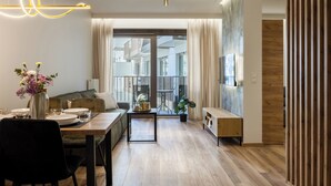 A modern living room with a dining area, a sofa, a coffee table, and a view through a glass door. -  LILY APART - Rooftop Terrace Apartments by the Shipyard (Gdansk)
