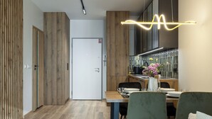 A modern kitchen with wooden cabinetry, a dining area with green chairs, and a visible door leading to another room. -  LILY APART - Rooftop Terrace Apartments by the Shipyard (Gdansk)