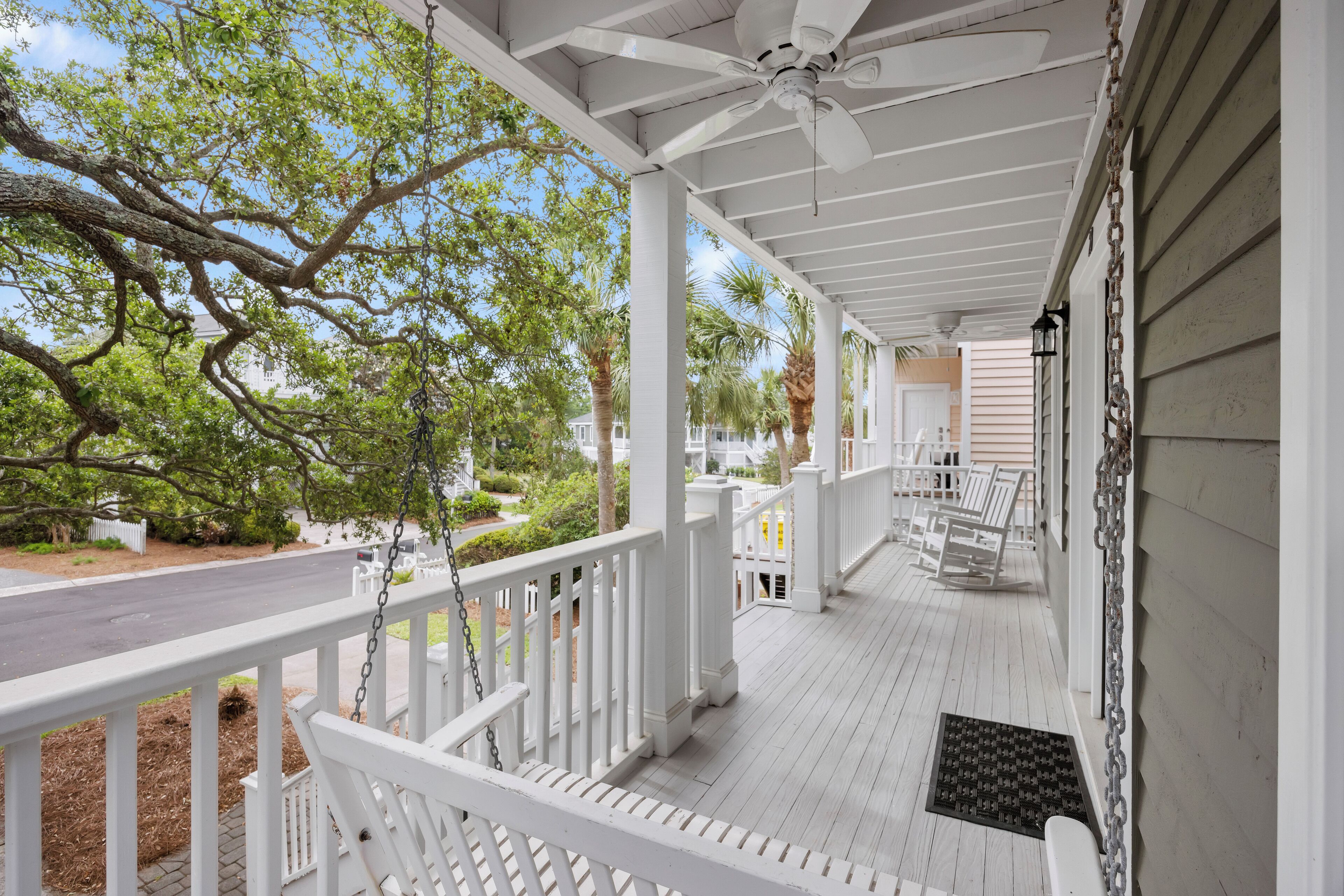 A covered porch with white railings, a ceiling fan, and a view of the street and trees.