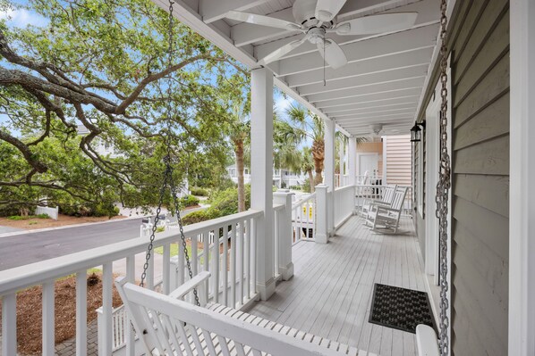 A covered porch with white railings, a ceiling fan, and a view of the street and trees.