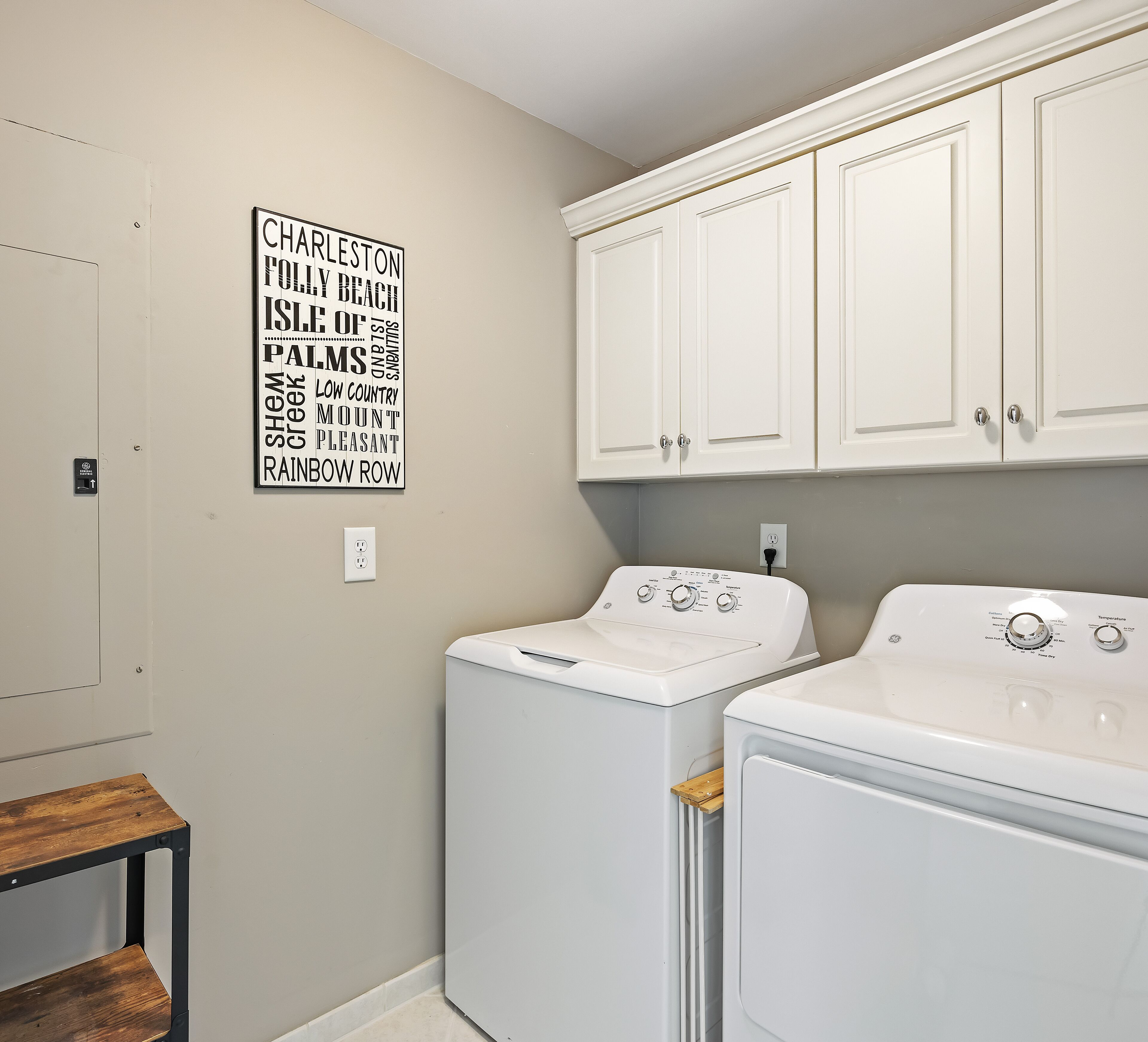 A laundry room with two white washing machines, a wooden bench, and a wall-mounted sign.
