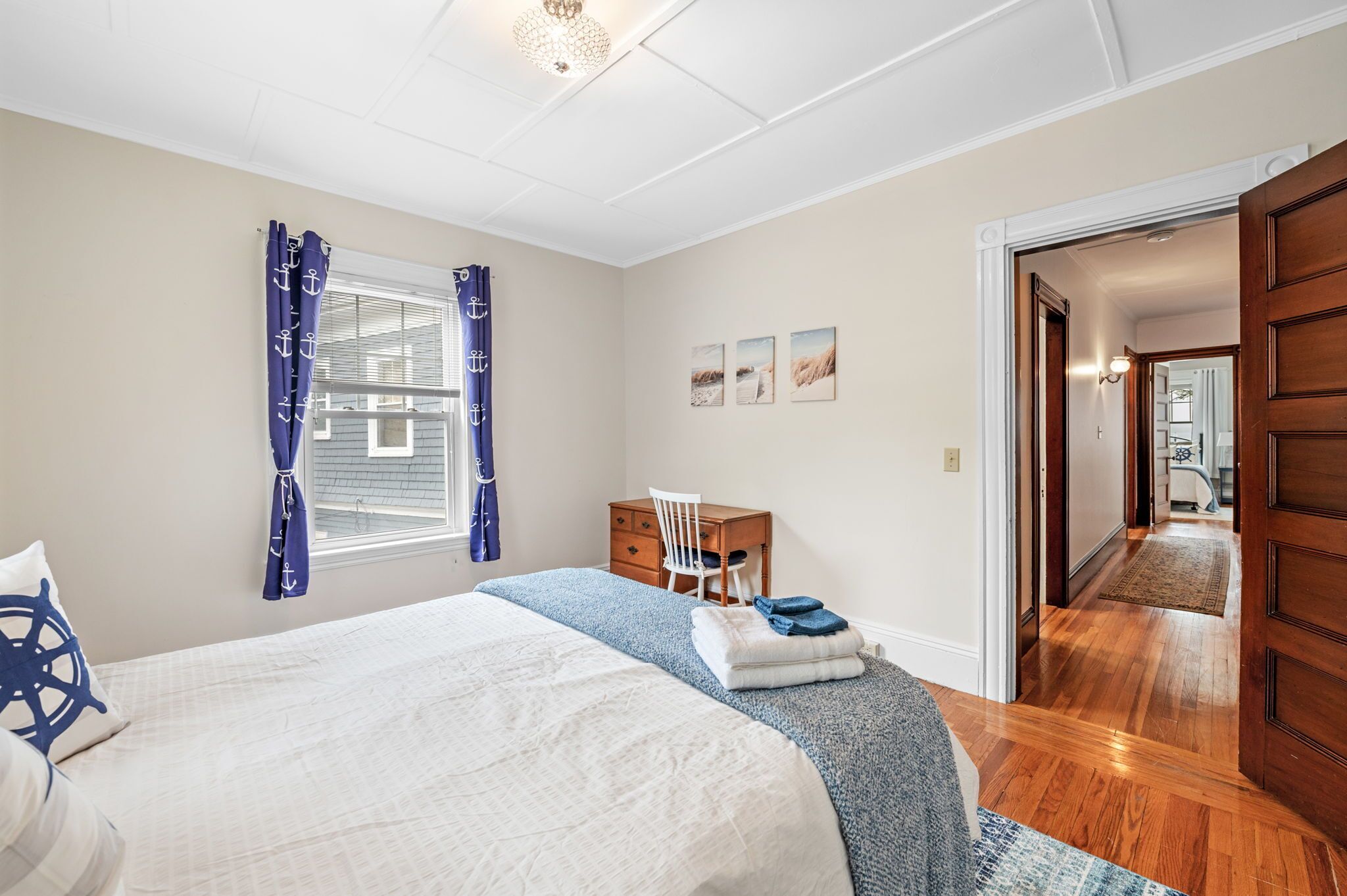 Quarto com cama, escrivaninha e cadeira. Cortinas na janela e porta que dá para outro cômodo.