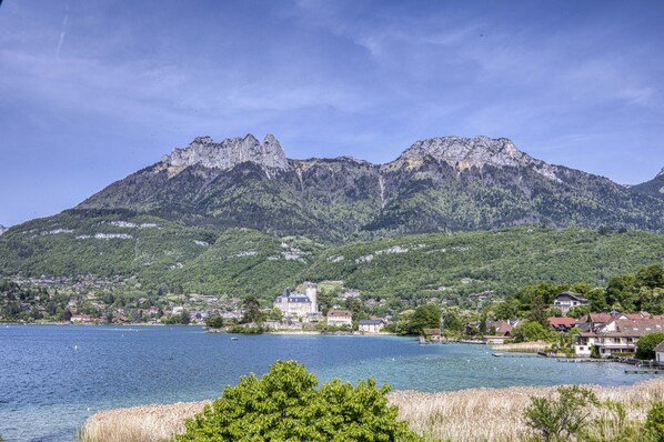 Un poble a la vora d'un llac, amb un castell destacat, envoltat d'unes verdes muntanyes i un cel blau clar.