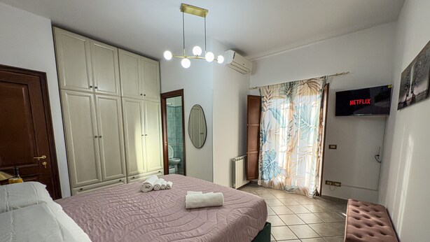 A bedroom with a bed, a wardrobe, a television, and a bathroom visible through an open door. - B&B La Fenice Rome - Fiumicino. Close to the center of Rome and the airport. (Lazio)