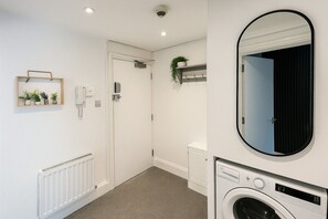 Une petite buanderie équipée d’un lave-linge, d’un radiateur, d’une porte et d’un miroir.