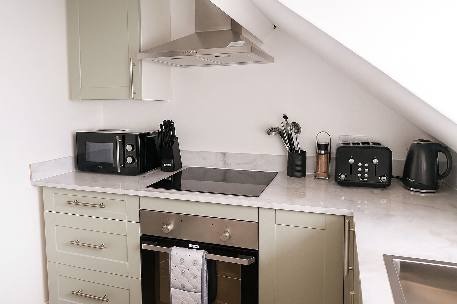 A compact kitchen with a built-in oven, a microwave, a toaster, and a kettle.
