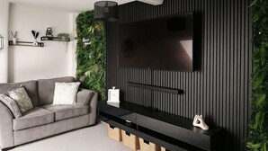 A modern living room with a grey sofa, a flat-screen TV mounted on a dark wall, and a vertical garden.