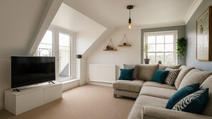 A modern living room with a sectional sofa, a flat-screen TV on a white cabinet, and a large window providing natural light.