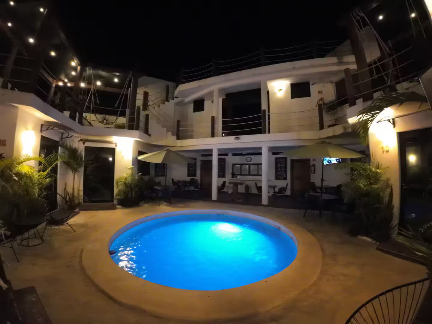 A circular pool with a blue center, surrounded by a covered patio area with tables and chairs.