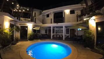 A circular pool with a blue center, surrounded by a covered patio area with tables and chairs.