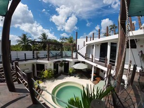 Uma área de piscina com uma piscina circular, um deck de madeira e um edifício branco com várias varandas.