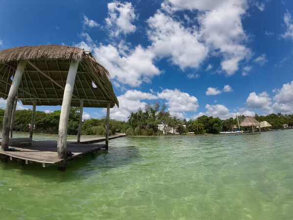 A wooden dock extending into clear turquoise water with a thatched-roof structure on it.
