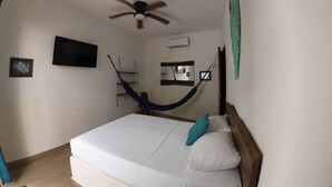 Un dormitorio con cama, ventilador de techo, televisión, hamaca y espejo.