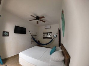 Um quarto com cama, ventilador de teto, televisão, rede e espelho.