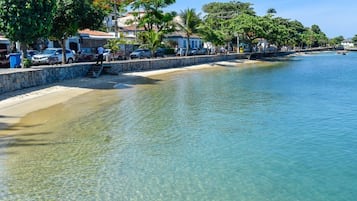 A coastal area with a clear waterfront, a stone wall, and parked cars along the side.