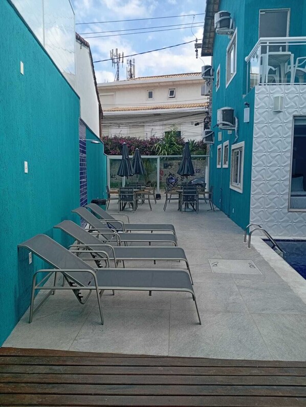 A poolside area with lounge chairs and umbrellas, a small pool, and a building with a teal exterior. - Pousada Menino do Rio (Buzios)