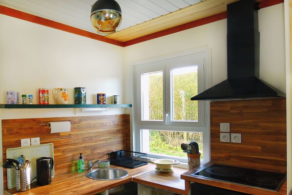 A kitchen with wooden cabinets, a black stove, a window with a view of greenery, and various kitchen items on the counter.