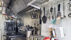 Una cocina comercial con electrodomésticos de acero inoxidable, incluyendo un microondas, estufa y varios utensilios colgados en la pared.