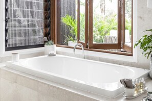 Bathroom features a large bathtub, window with bamboo blind, and a potted plant.