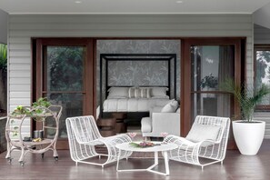 Relax in this serene bedroom with a large bed, wicker chairs, and a potted plant, offering a peaceful retreat with a balcony view.