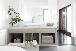 Bathroom features a large vessel sink, mirror, and potted plant, with wicker baskets and toiletries below.