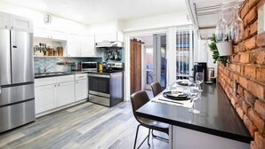Une cuisine moderne dotée d’appareils électroménagers en acier inoxydable, un coin repas agrémenté d’un mur en briques apparentes et une porte-fenêtre coulissante donnant sur un espace extérieur.