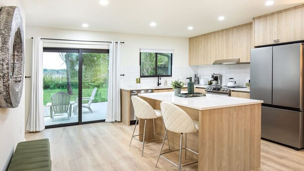 A modern kitchen with a central island, bar stools, a large refrigerator, and a sliding glass door leading to a patio with outdoor seating. - ` Velvet Bloom ` unique location 3mil to Downtown (Naples)
