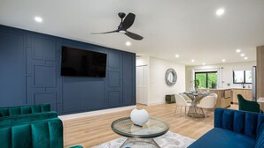 A modern living room with a flat-screen TV, dark blue walls, and a ceiling fan. - ` Velvet Bloom ` unique location 3mil to Downtown (Naples)
