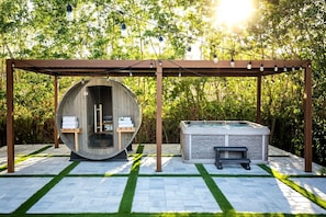 Un jacuzzi bajo una pérgola adornada con luces, rodeado de un patio de piedra y follaje.