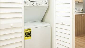 A laundry room with a front-loading washer and dryer, a yellow energy guide sticker, and a wooden floor.