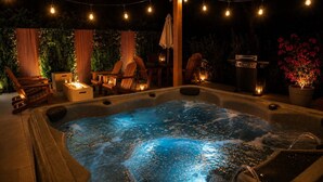 Ein Whirlpool mit Holzterrasse, umgeben von Stühlen und Topfpflanzen, unter Lichterketten.