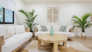 Ein modernes Wohnzimmer mit einem weißen Sofa, einem runden Couchtisch aus Holz und zwei Blumentöpfen.