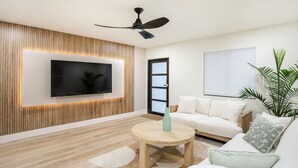 Ein modernes Wohnzimmer mit einem an einer Holzwand montierten Flachbildfernseher, einem Deckenventilator, einem weißen Sofa, einem runden Couchtisch aus Holz und einer Topfpflanze.