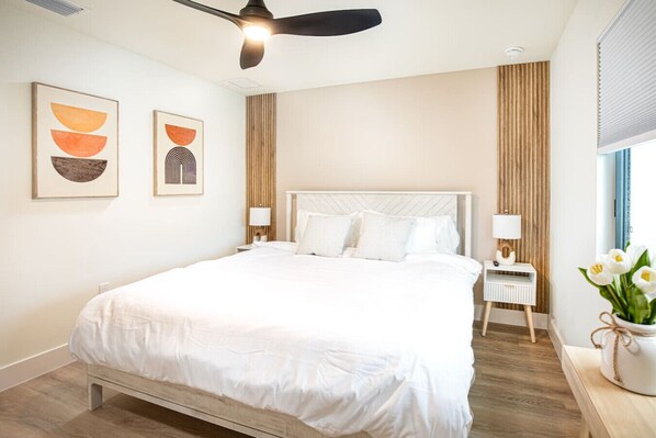 A modern hotel room with a large bed, a ceiling fan, two bedside tables with lamps, and artwork on the wall.