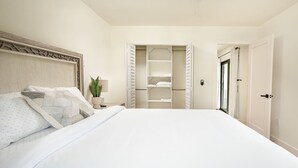A bedroom with a large bed, a nightstand with a lamp, a potted plant, and a walk-in closet with shelves. - ` The Black Vanilla ` Luxe Retreat Sauna, Cold Plunge & Pure Relaxation (Naples)