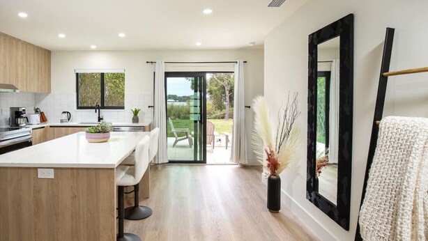 A modern kitchen with a central island, a dining area, and a large sliding glass door leading to an outdoor patio. - ` The Black Vanilla ` Luxe Retreat Sauna, Cold Plunge & Pure Relaxation (Naples)